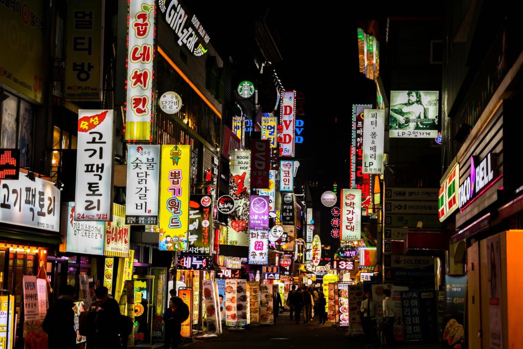 a street with signs and people walking in the dark with Kabukichō, Tokyo in the background
